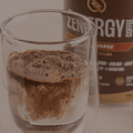 Vaso con Zenergy Chocolate Belga en polvo y envase al fondo