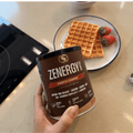 Envase de Zenergy Chocolate Belga junto a gofres y fresas en una mesa